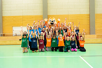 Eine Gruppe Kinder ist mit dem Maskottchen der hessischen Turnjugend zu sehen.