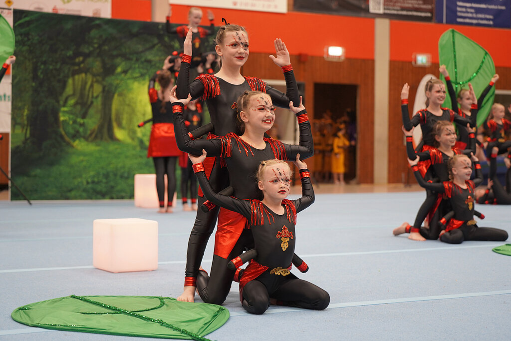 Drei Mädchen aus einer Showgruppe in rot-schwarzen Kostümen zeigen eine Figur.