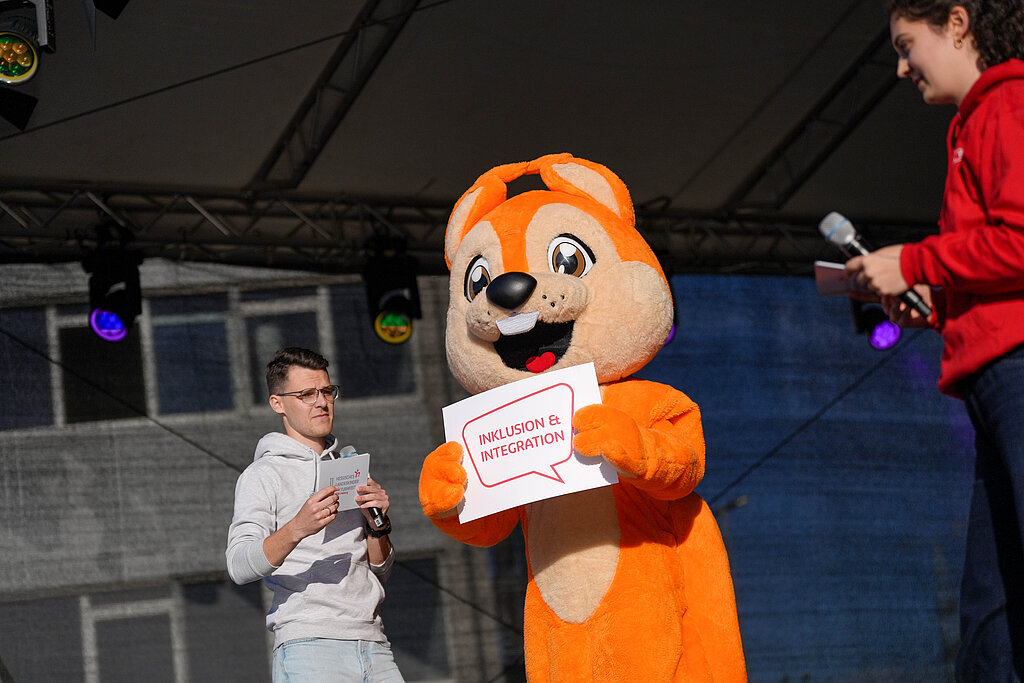 Das Maskottchen Freddy, ein Eichhörnchen, hält auf der Bühne ein Schild hoch.