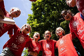 Kinder in einem roten Trikot stehen in einem Kreis und lachen