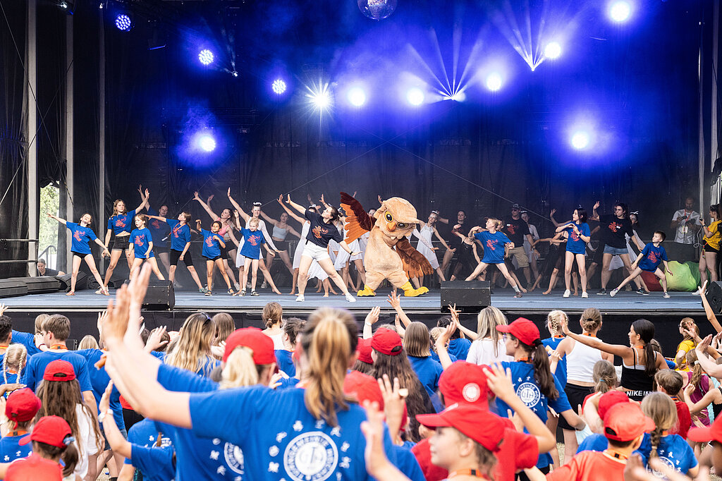 [Translate to Einfache Sprache:] Vor und auf einer Bühne tanzen viele Menschen.