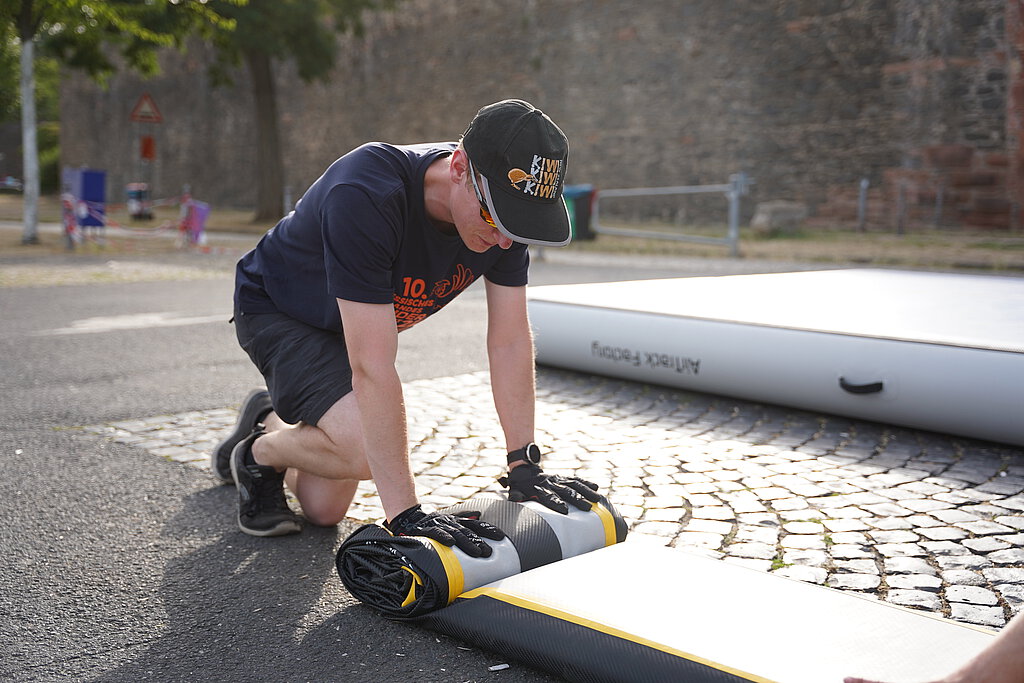 Eine Person in Arbeitskleidung und Turnfest-Design rollt eine Plane zusammen.