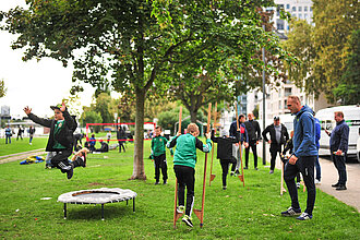 Familien mit Kindern spielen mit Sportmaterialien in einem Park auf einer Wiese.