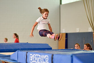 Mädchen springt in einer Halle auf einem großen Trampolin.