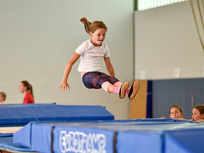 Mädchen springt in einer Halle auf einem großen Trampolin.