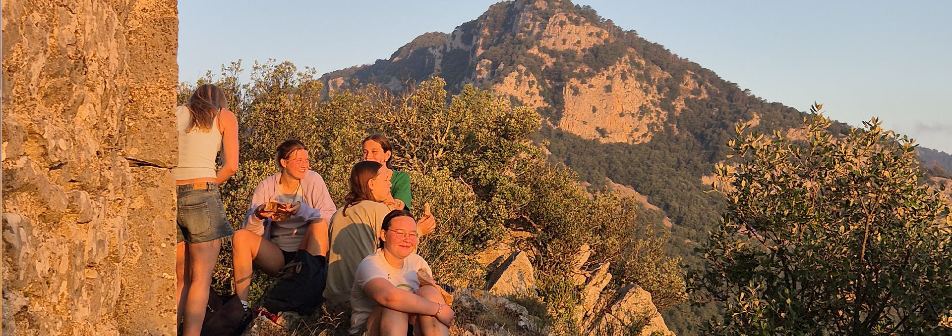Jugendliche sitzen bei Sonnenuntergang auf einem Felsen.